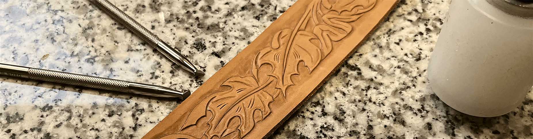 Zdobený kožený proužek s paličkou a raznicemi v pozadí